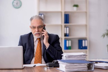 Old employee speaking by phone at workplace