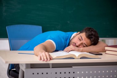 Genç öğretmen yeşil panonun önünde.