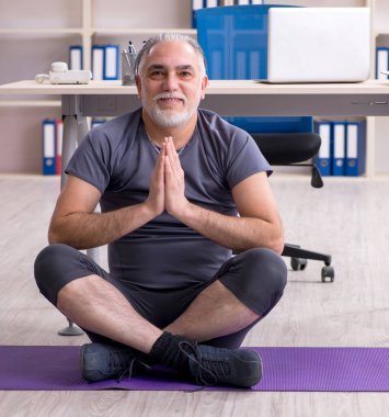 Ofiste egzersiz yapan beyaz sakallı yaşlı adam.