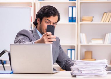 The young handsome employee in wheelchair at the office