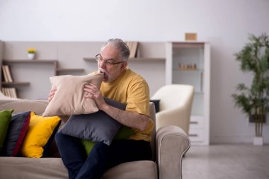Evde bir sürü yastığı olan yaşlı bir adam.