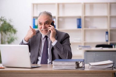 Old employee speaking by phone at workplace