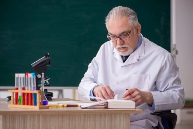 Old chemist teacher sitting in the classroom