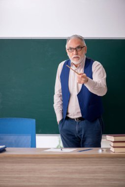Eski öğretmen yeşil panonun önünde.