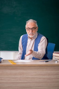 Eski öğretmen yeşil panonun önünde.