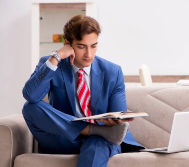 Evde çalışan genç işadamı kanepede oturuyor.