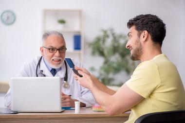 Genç hasta yaşlı doktoru ziyaret ediyor.