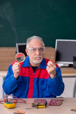 Sınıfta bilgisayar tamir eden yaşlı bir erkek tamirci.