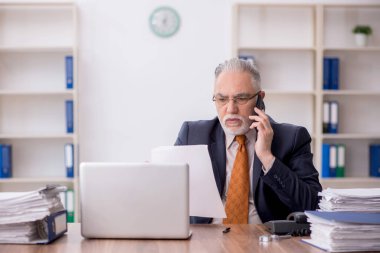 Old employee speaking by phone at workplace