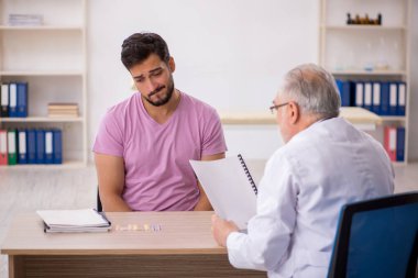 Genç hasta yaşlı erkek doktoru ziyaret ediyor.