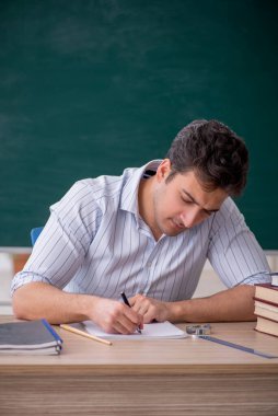 Genç öğretmen yeşil panonun önünde.