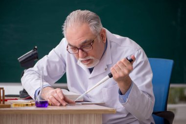 Old chemist teacher sitting in the classroom