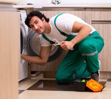 Genç müteahhit mutfakta çamaşır makinesini tamir ediyor.