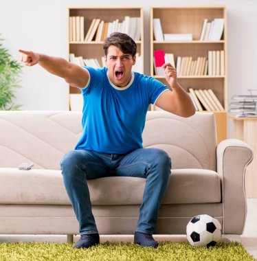 Evde kanepede oturup futbol izleyen adam.