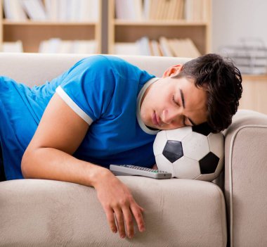 Evde kanepede oturup futbol izleyen adam.