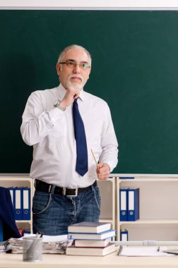 Tahtanın önündeki yaşlı erkek öğretmen.