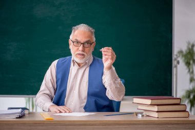 Eski öğretmen yeşil panonun önünde.