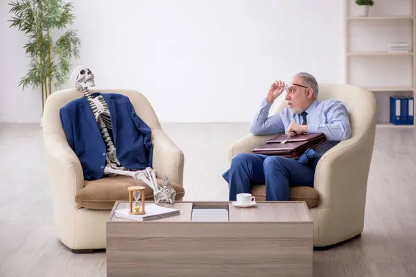 Old male boss and skeleton in business meeting concept