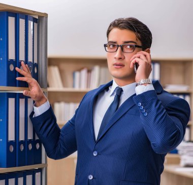 Elinde dosyalarla rafın yanında duran genç adam.