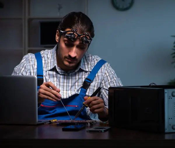 Young technician repairing computer in workshop at night