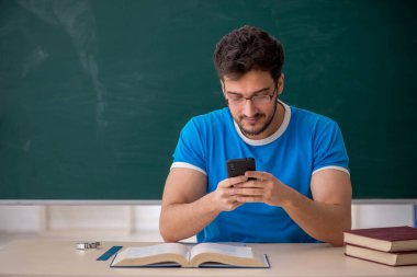 Sınıfta akıllı telefon tutan genç bir öğrenci.