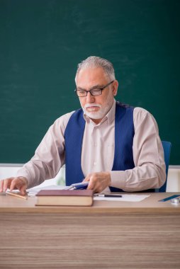 Eski öğretmen yeşil panonun önünde.