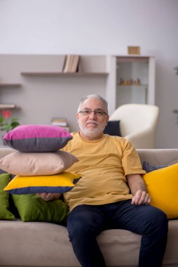 Evde bir sürü yastığı olan yaşlı bir adam.
