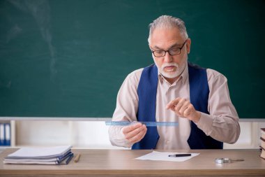 Eski öğretmen yeşil panonun önünde.