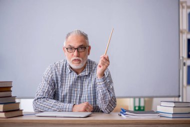 Yaşlı öğretmen beyaz tahtanın önünde oturuyor.