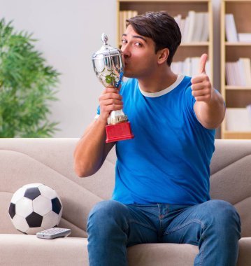 Evde kanepede oturup futbol izleyen adam.