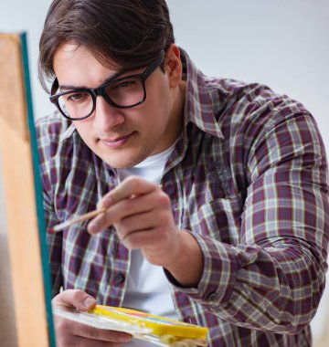 Genç erkek sanatçı parlak stüdyoda resimler çiziyor.