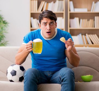 Evde kanepede oturup futbol izleyen adam.