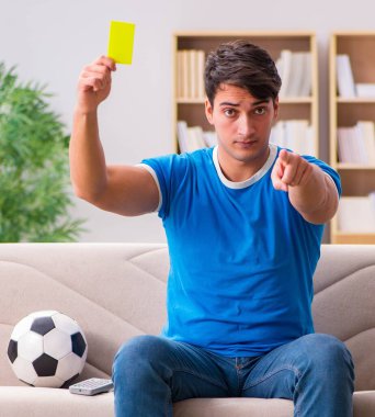 Evde kanepede oturup futbol izleyen adam.