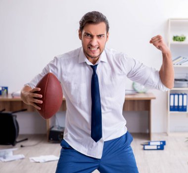 Genç bir çalışan ofiste rugby topu atıyor.