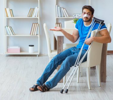 Genç adam ameliyattan sonra koltuk değnekleri ve tekerlekli sandalyeyle iyileşiyor.