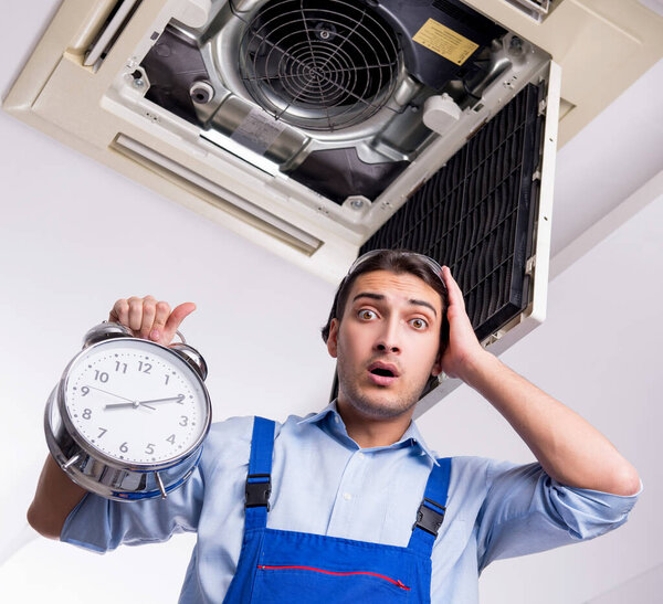 Молодой ремонтник ремонтирует потолочный кондиционер