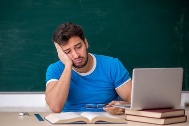 Genç öğretmen yeşil panonun önünde.