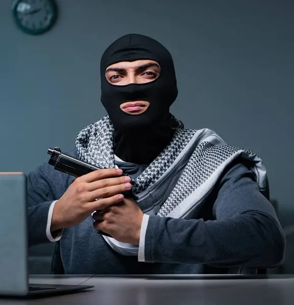 The terrorist burglar with gun working at computer