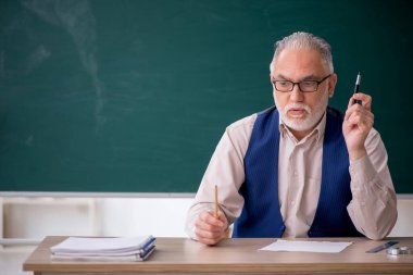 Eski öğretmen yeşil panonun önünde.
