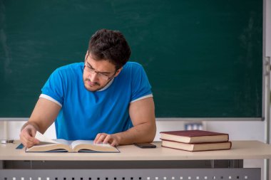 Genç öğretmen yeşil panonun önünde.