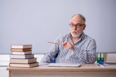 Yaşlı öğretmen beyaz tahtanın önünde oturuyor.