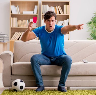 Evde kanepede oturup futbol izleyen adam.
