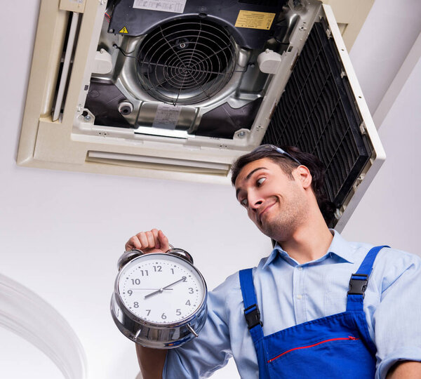 Молодой ремонтник ремонтирует потолочный кондиционер