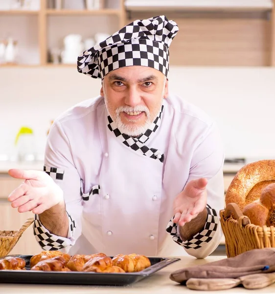 The old male baker working in the kitchen