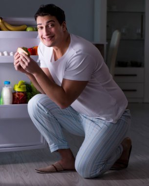 Buzdolabının başındaki adam gece yemek yiyor.