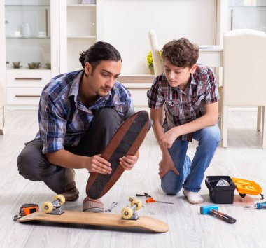 Genç baba oğluyla birlikte kaykay tamir ediyor.