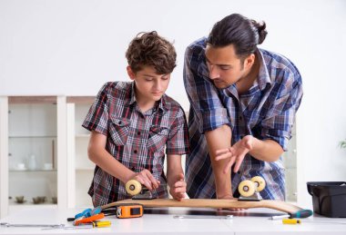 Genç baba oğluyla birlikte kaykay tamir ediyor.