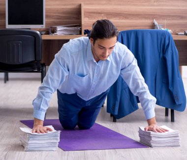 Genç yakışıklı işadamı iş yerinde egzersiz yapıyor.