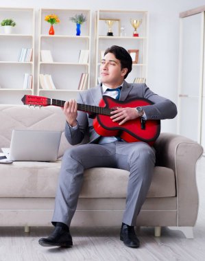 Evde gitar çalan iş adamı.