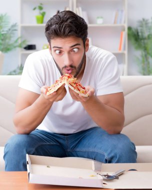 Pizza yiyen adam evde yemek yiyor, dinleniyor.